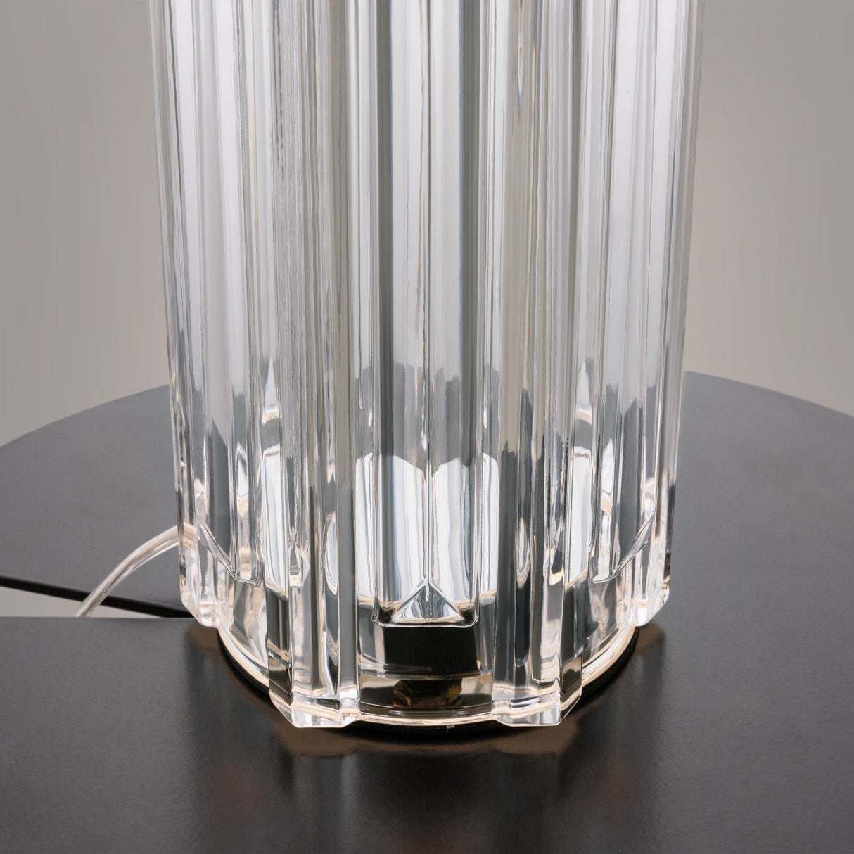 A close-up of the Muse Table Lamp - Chrome With White Shade reveals its modern design with translucent vertical ridges. It sits on a dark surface, enhancing its sleek, minimalist aesthetic with a visible power cord at the chrome base—perfect for contemporary interiors.