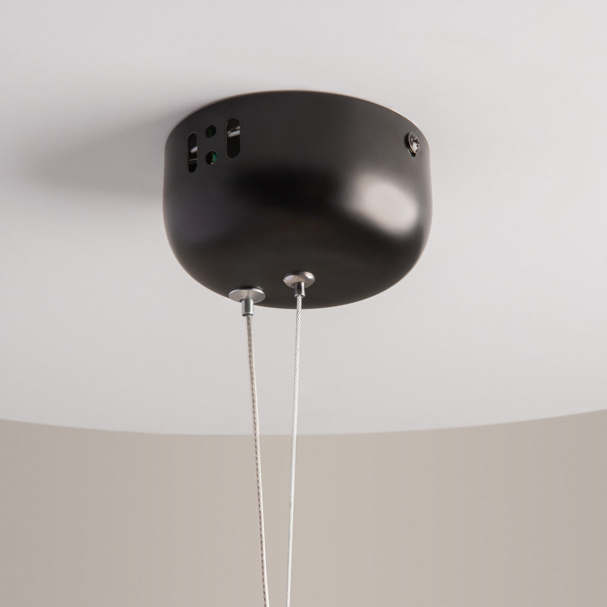 The Rebel LED Glass Pendant Light - Gold has a dome-shaped black fixture with two cables, mounted on a white ceiling. It features small ventilation openings, a circular cap with screws, and provides an energy-efficient LED light source for modern elegance.
