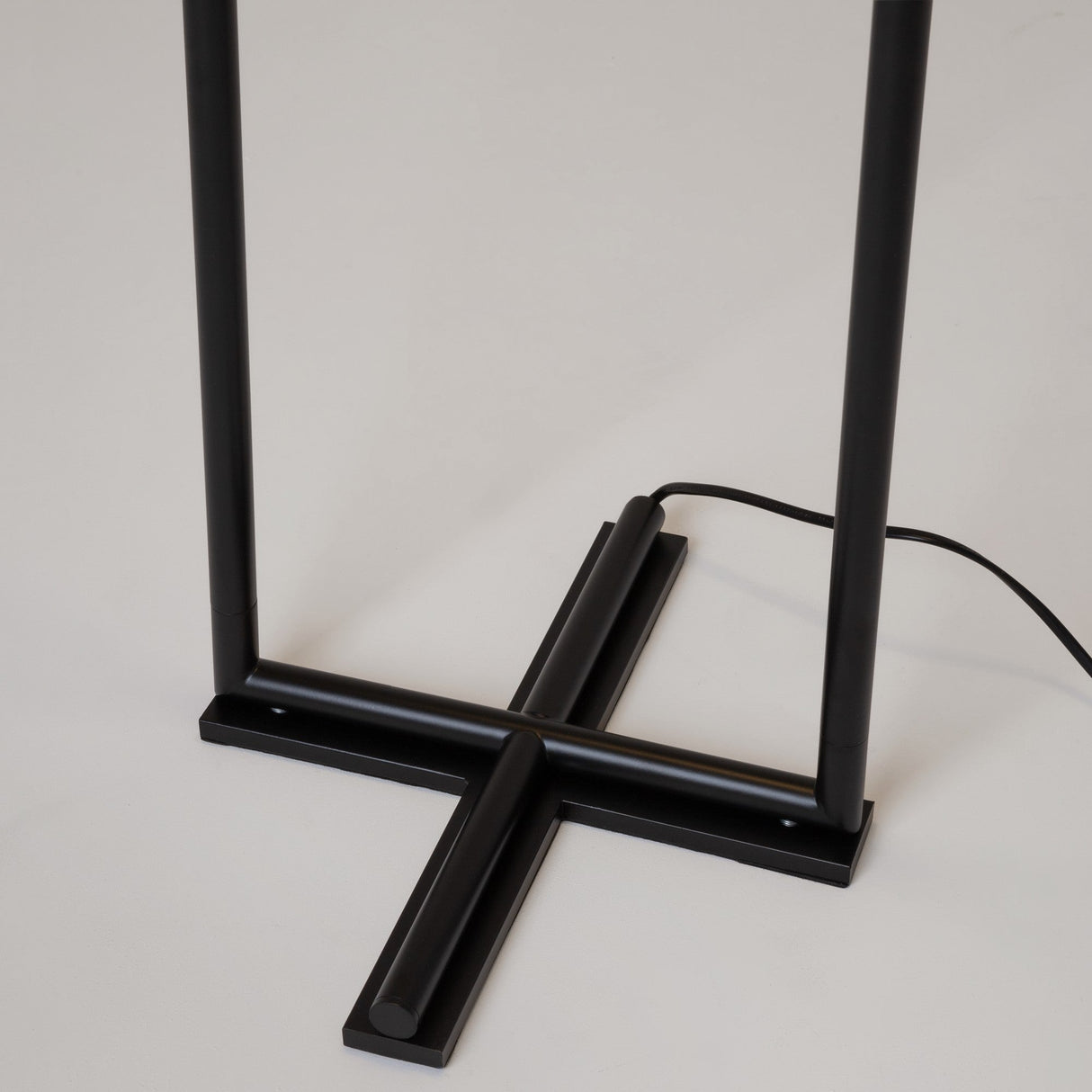 Close-up of The Sixth Sense 2 Light LED Floor Lamp 3000K 12W in black with a sleek metal stand and cross-shaped base on a light floor. A cord extends from the base, highlighting its minimalist design and contemporary decor appeal.