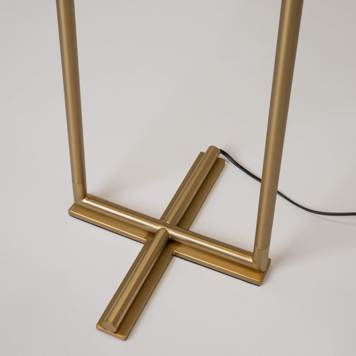 Close-up of The Sixth Sense 2 Light LED Floor Lamp, showcasing its unique cross-shaped brass base with a black cord, contrasting the light background to enhance ambient lighting.