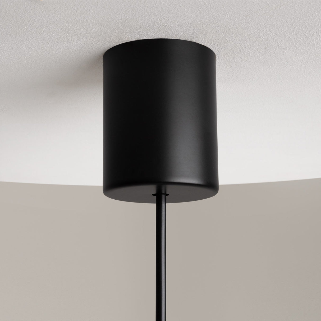 The Sixth Sense LED Pendant Light, featuring a modern black cylindrical design with a matte finish and white glass, is mounted on the ceiling. The sleek fixture enhances its minimalist appeal as it hangs elegantly.