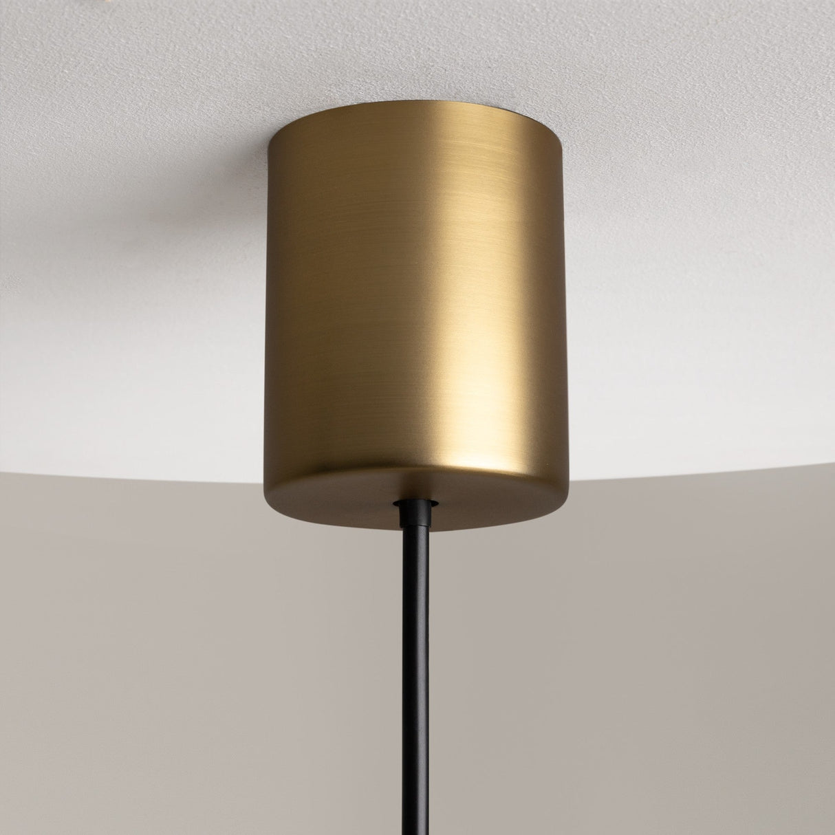 Close-up of The Sixth Sense LED Pendant Light 3000K 7W featuring a brass finish and white glass. A black rod extends downward, complementing its modern look against a white ceiling and neutral-toned wall.