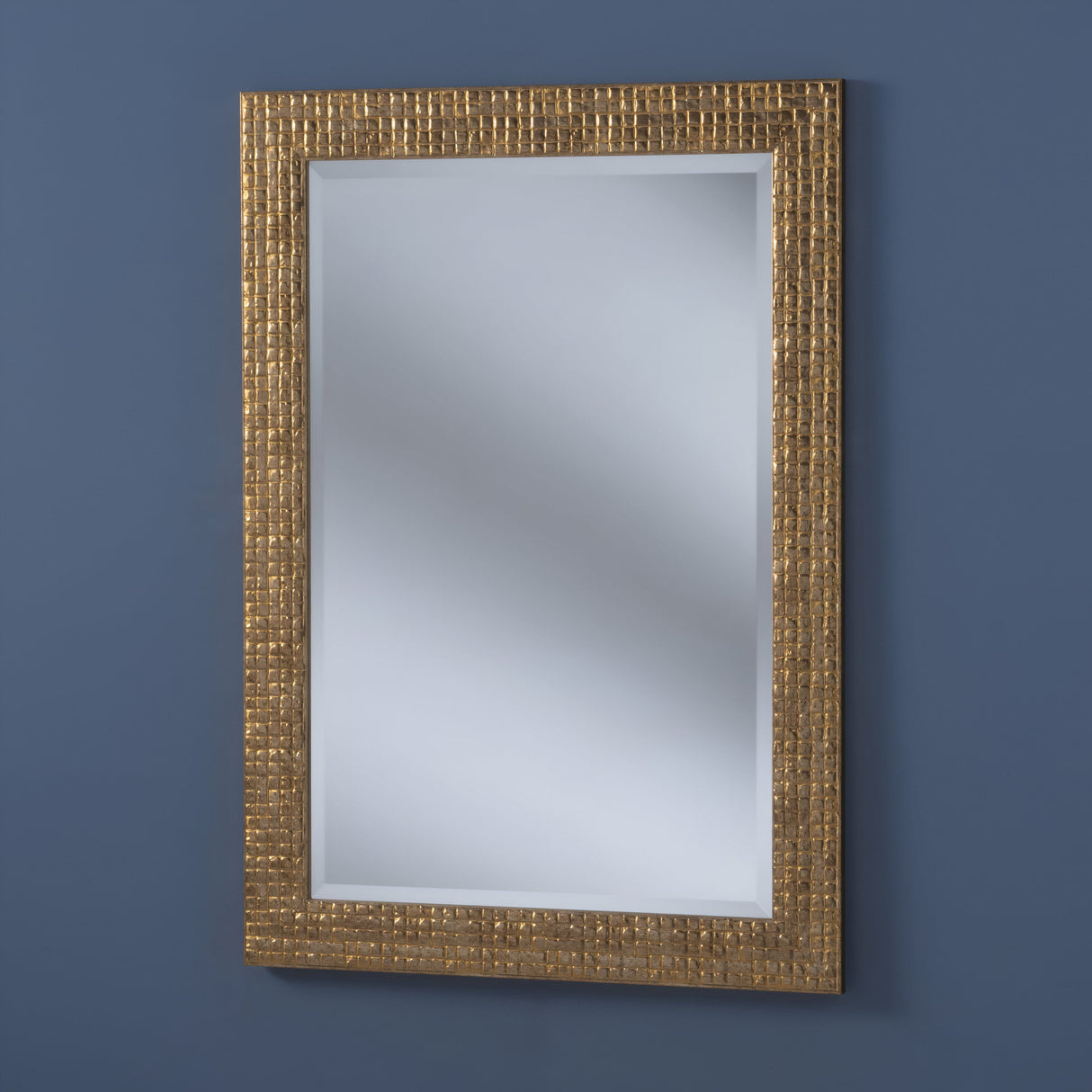 The Iridessa Rectangle Wall Mirror - Gold hangs on a dark blue wall, reflecting light with its textured gold frame. Its simple yet elegant design enhances the sophistication of your luxury home decor.