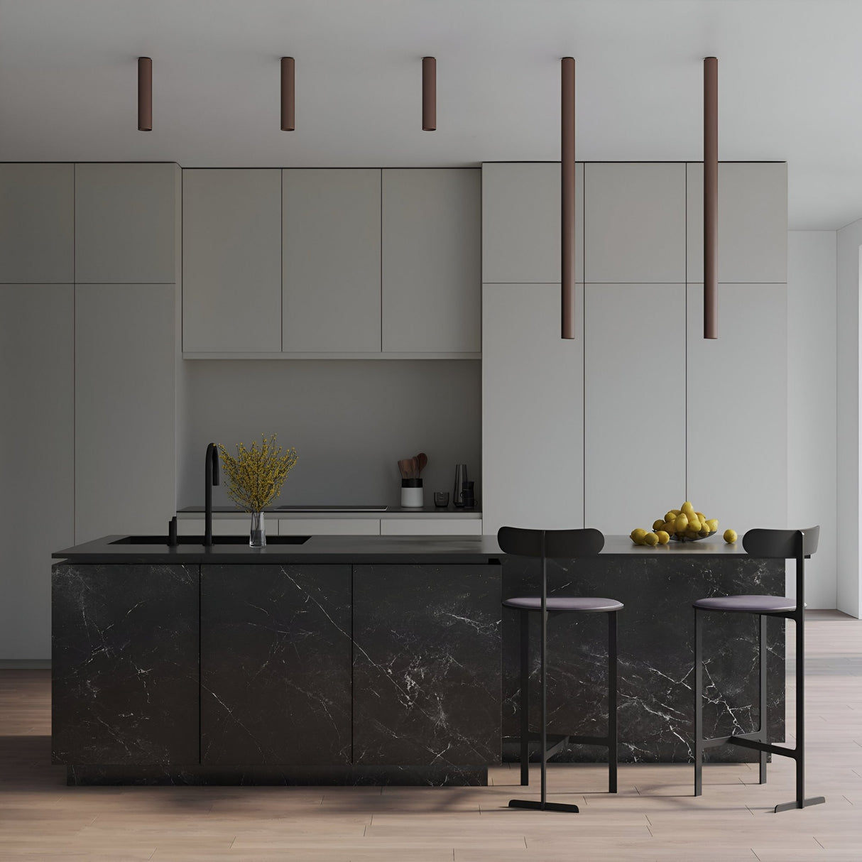 Minimalist modern kitchen with light gray cabinets, a black marble island, and two black barstools. Four Pulcra Tube Ceiling Lights in copper hang above the island, which displays a vase of yellow flowers and a bowl of lemons.