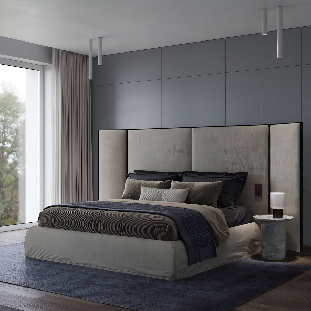 A modern bedroom with a large upholstered bed, dark bedding, and plush pillows exudes minimalist elegance. The Pulcra Tube Ceiling Light - White with its sleek design complements the round bedside table as soft natural light filters through the curtains.