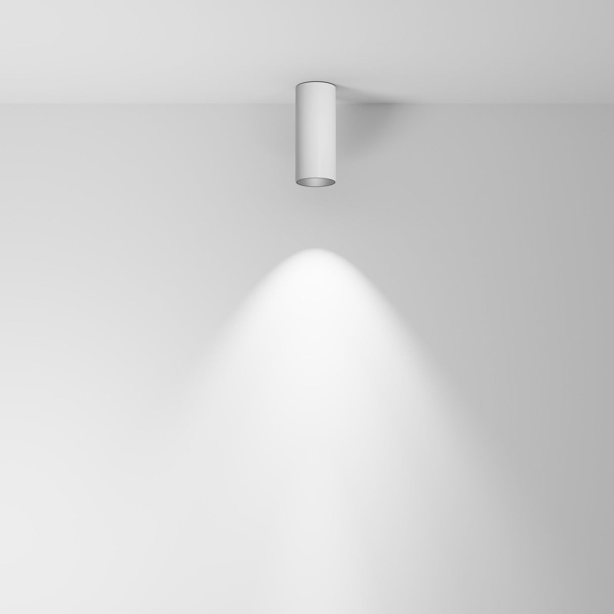 The Focus LED Fixed Round Surface Mounted Downlight 12W 3000K in white casts a soft, focused beam downward onto a plain white wall and ceiling, creating a symmetrical triangular pattern. This energy-efficient lighting enhances the bright, uncluttered environment.
