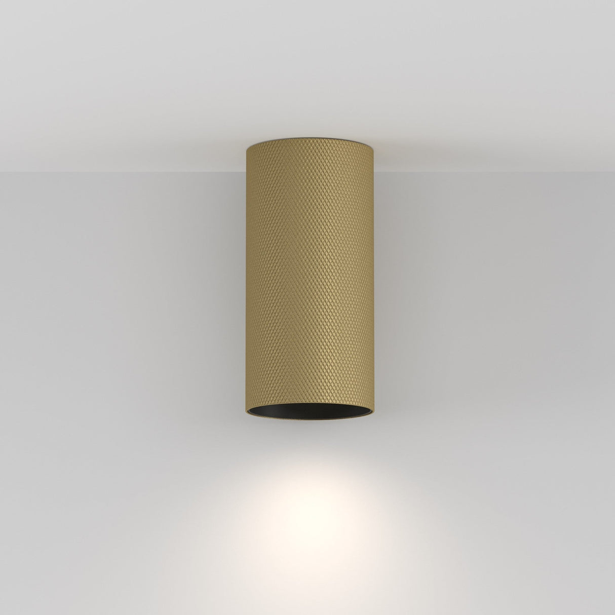 A cylindrical matte gold ceiling light fixture mounted on a white ceiling, casting a warm glow downward—an embodiment of luxury lighting with the Artisan Single Fixed Round Surface Mounted Downlight.