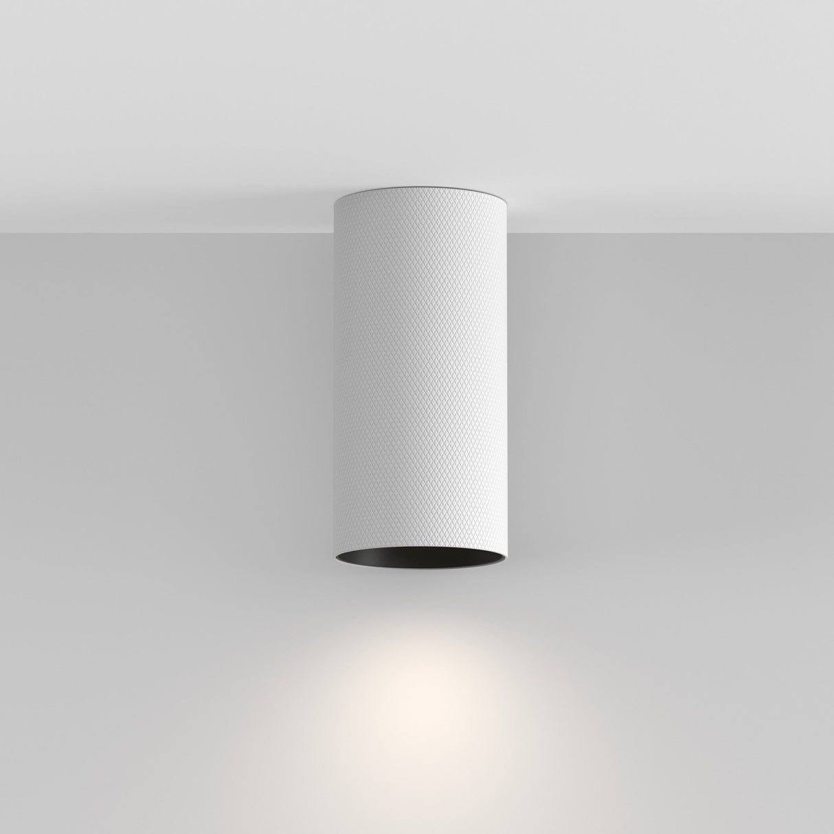 The Artisan Single Fixed Round Surface Mounted Downlight in white is a minimalist cylindrical light fixture with a sleek finish, elegantly attaching to the ceiling and casting a soft glow onto the wall below.