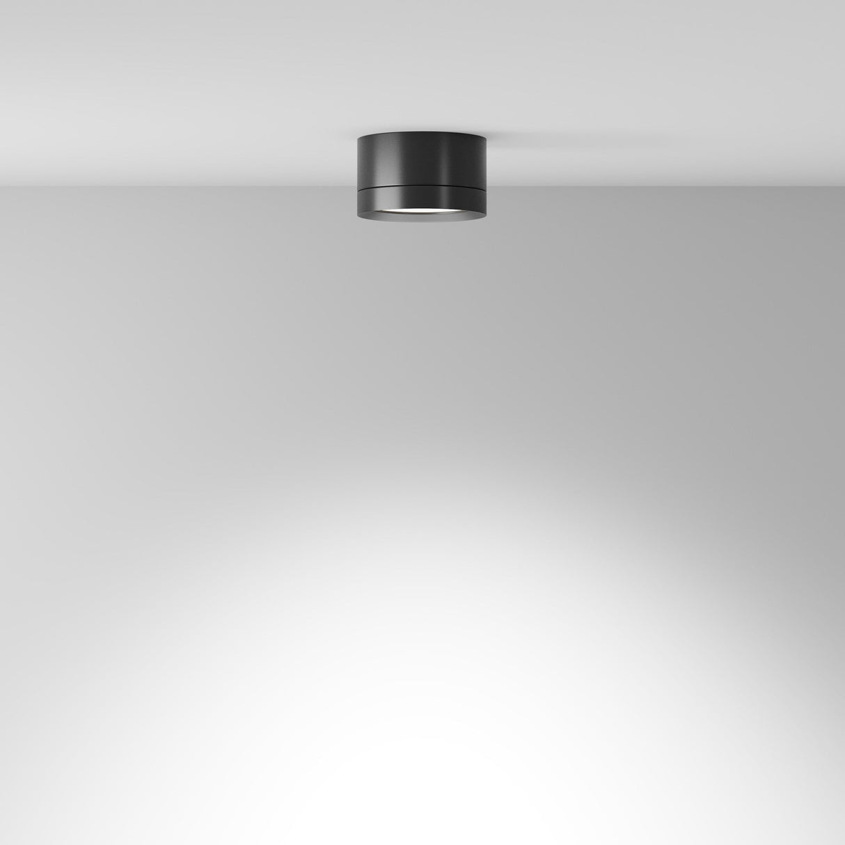 The black Hoop Small Round Surface Downlight, mounted on a white ceiling, adds modern elegance by casting a subtle glow on the ceiling and wall, enhancing the rooms sleek and uncluttered charm.