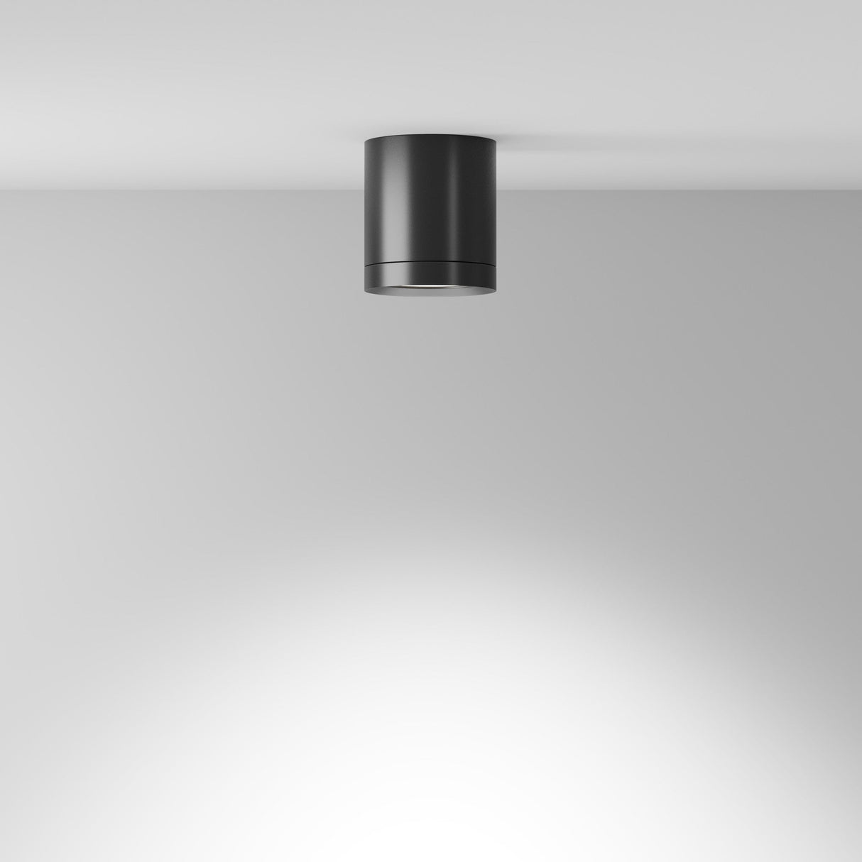 The Hoop Medium Round Surface Downlight in black is mounted on a white ceiling. This energy-efficient LED casts gentle illumination with a subtle gradient effect. Its sleek and minimalist design complements modern interiors perfectly.