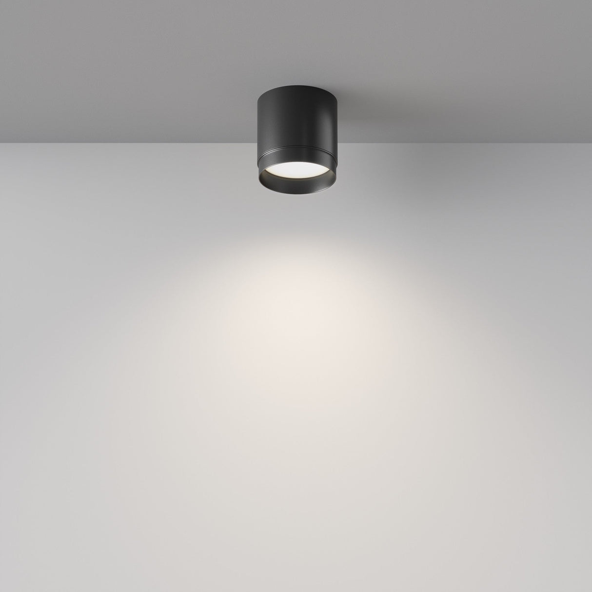 The Polar Round Surface Downlight - Black is elegantly mounted on a white ceiling, enhancing modern interiors by casting a focused circle of light onto the adjacent white wall.