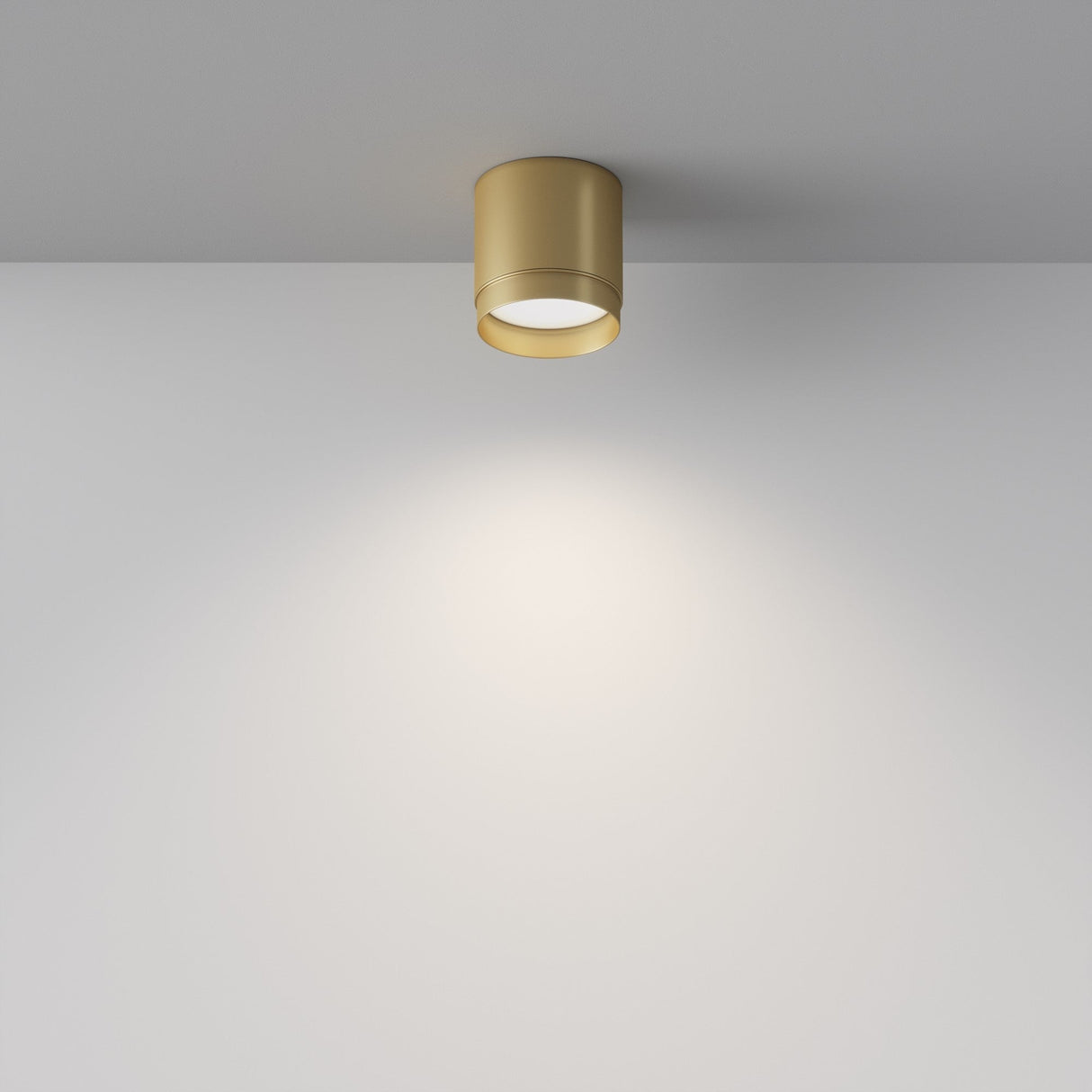 The Polar Round Surface Downlight in Matte Gold casts a soft, circular glow on a white wall, with its minimalist design contrasting against the plain backdrop to create a modern and elegant ambiance.