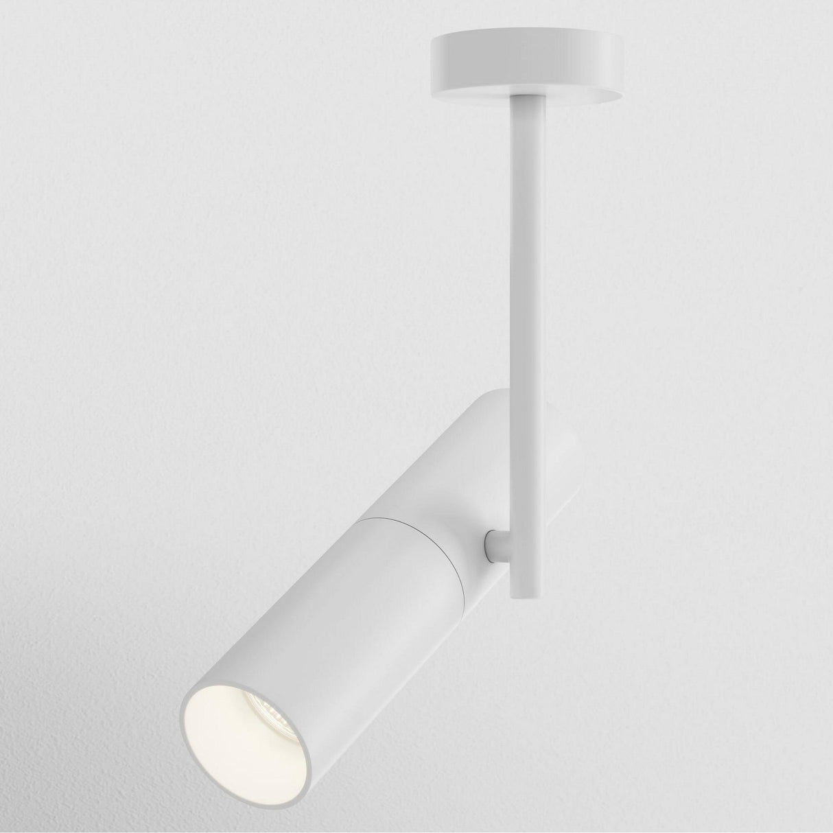 The Elti Single Spotlight - White is a sleek, modern ceiling fixture with a cylindrical design on a round base, showcasing minimalist style. Its pivoting head allows for customizable lighting, casting a focused beam against the smooth white wall.