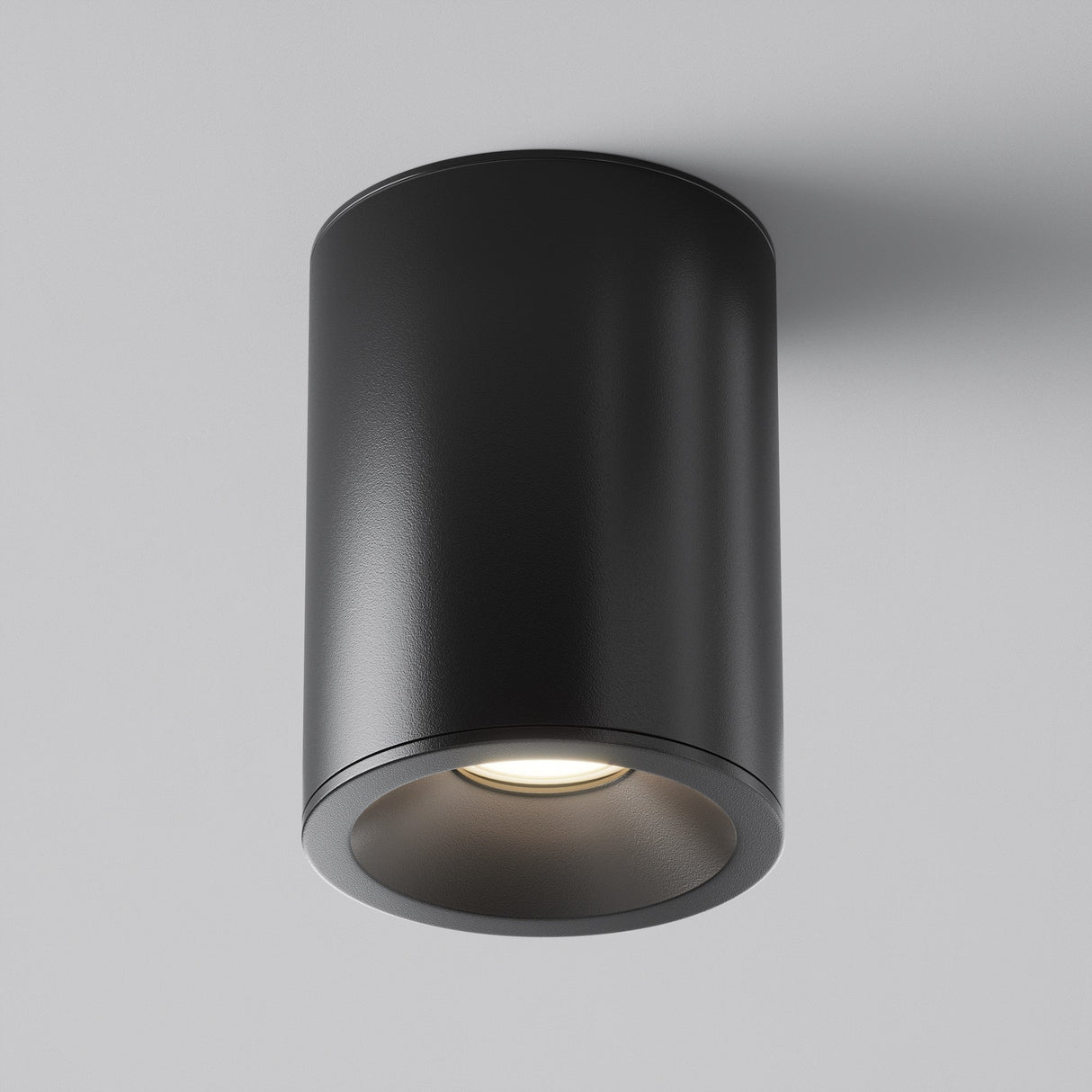 The Zoom Round Surface Downlight - Black features a cylindrical matte black design with a small circular opening emitting warm white light. Set against a white background, it offers durability with an IP65 rating.