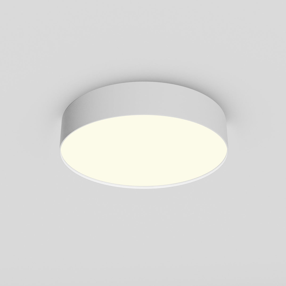 The Zon LED Small Flush Ceiling Light 3000K 36W - White is installed on a light gray ceiling. It emits a soft, even glow with its minimalist and modern design when turned on.