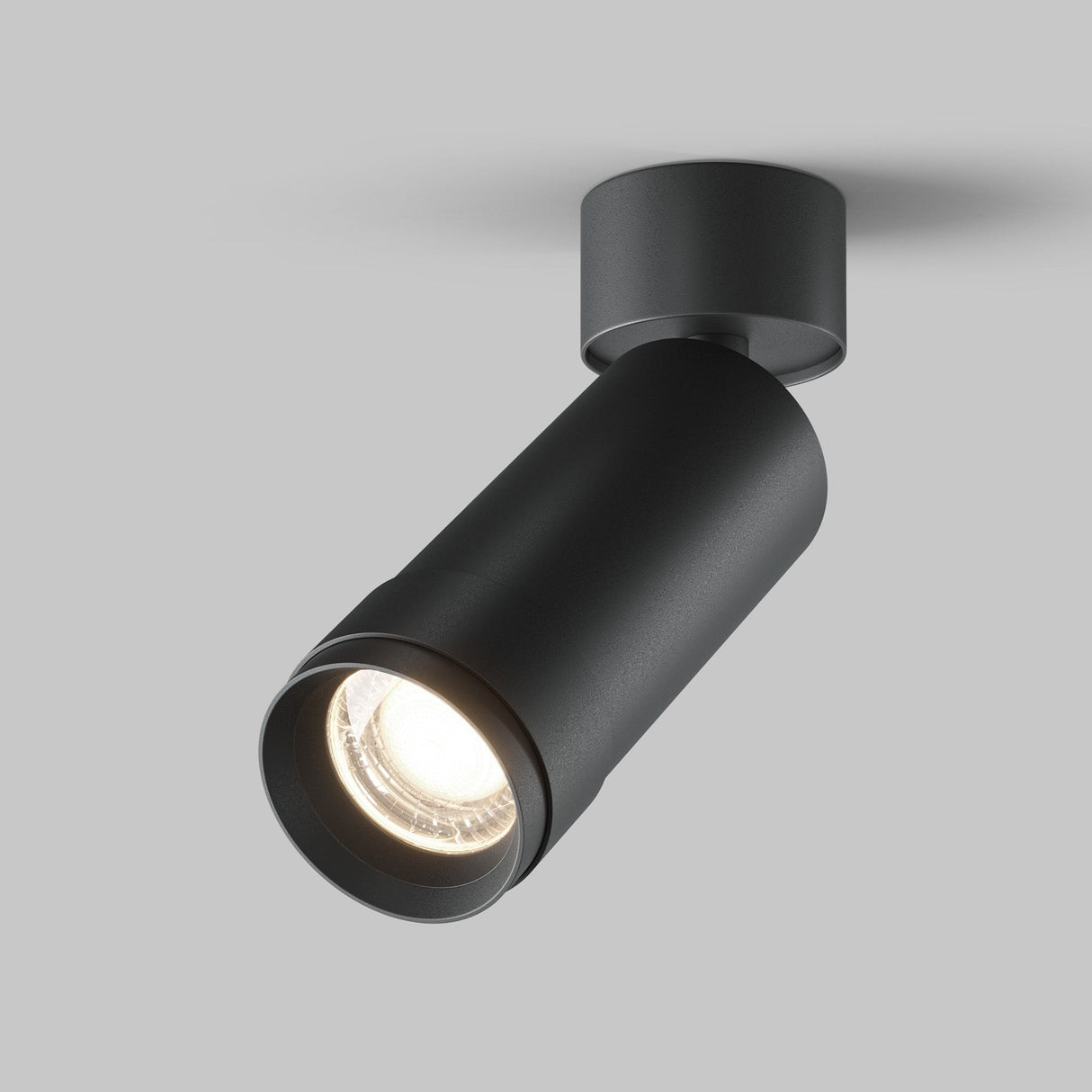 The Focus Zoom LED Single Surface-Mounted Spotlight 12W 4000K in black, with high CRI for true color representation, is angled downward against a plain gray background, switched on and emitting a bright light from its circular lens.