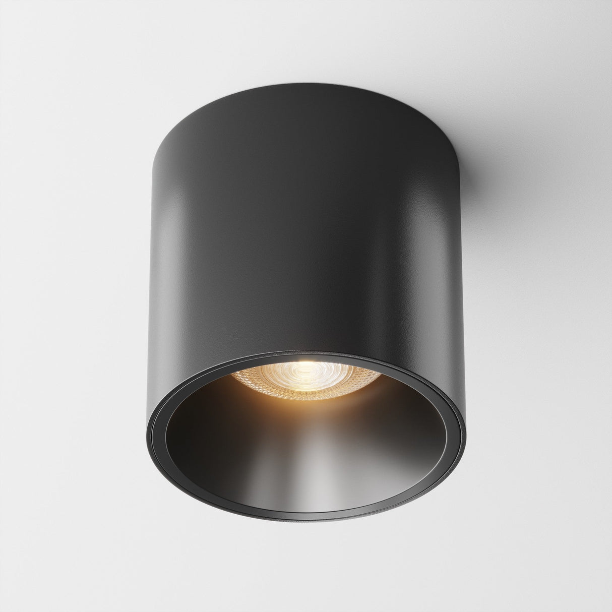 The Alfa LED Round Surface Downlight 12W 3000K in black is mounted on a white ceiling, offering a sleek, minimalist design with clean lines and a warm LED glow.