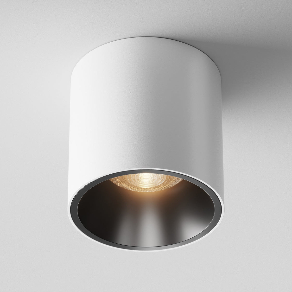The Alfa LED Round Surface Downlight 12W 3000K - White & Black features a ceiling-mounted cylindrical design with a recessed warm white light, creating a striking contrast against darker interiors, making it ideal for modern spaces.