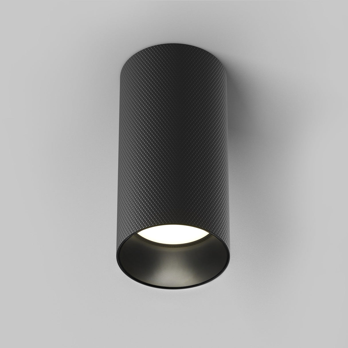 The Artisan Single Fixed Round Surface Mounted Downlight in Black features a cylindrical, textured design, casting a soft downward glow against a plain gray backdrop, exemplifying contemporary style.