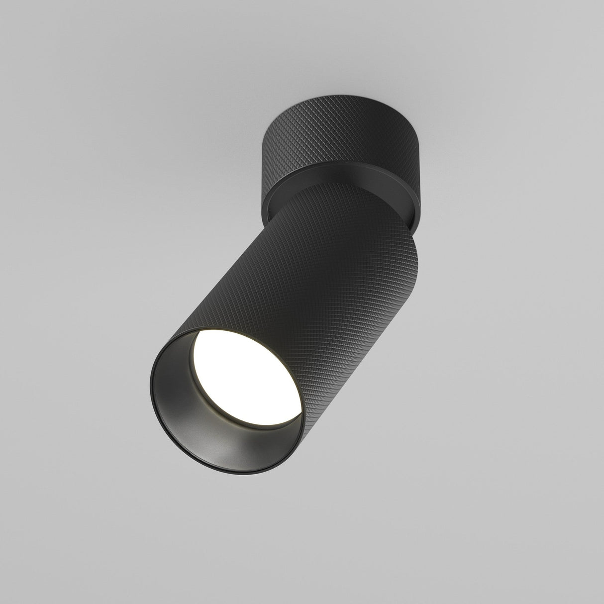 The Artisan Single Spotlight - Black, with its textured cylindrical design, is mounted on a white ceiling. It casts a soft glow and appears adjustable, offering a customizable lighting solution ideal for fans of minimalist design.