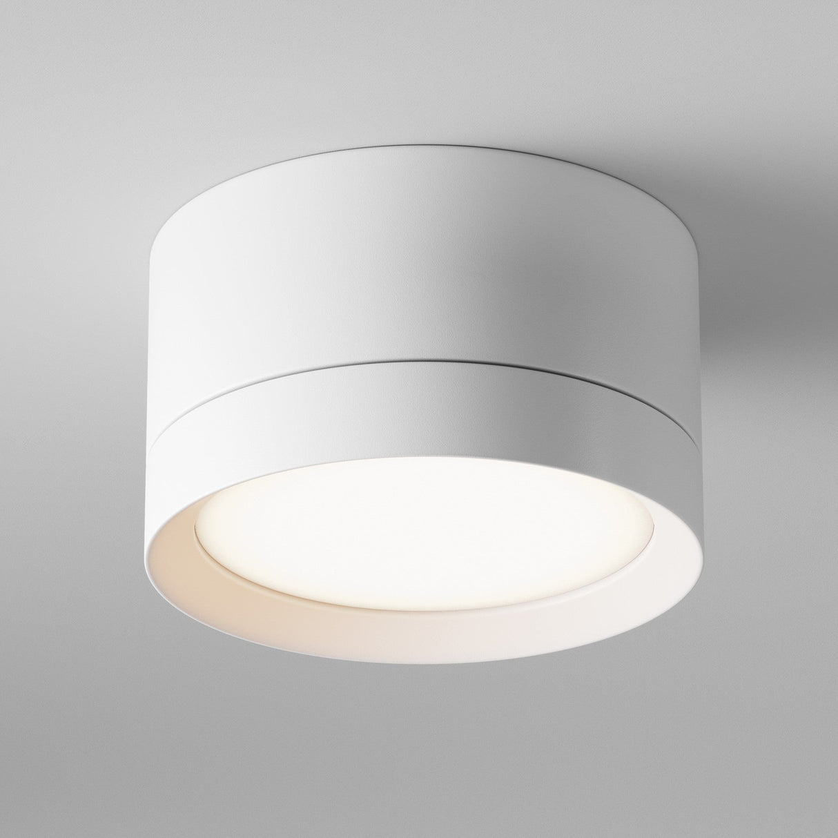 The Hoop Small Round Surface Downlight in white is mounted on a smooth, light-colored ceiling. This energy-efficient LED fixture casts a soft glow from its bottom opening, perfectly highlighting its minimalist design for modern interiors.