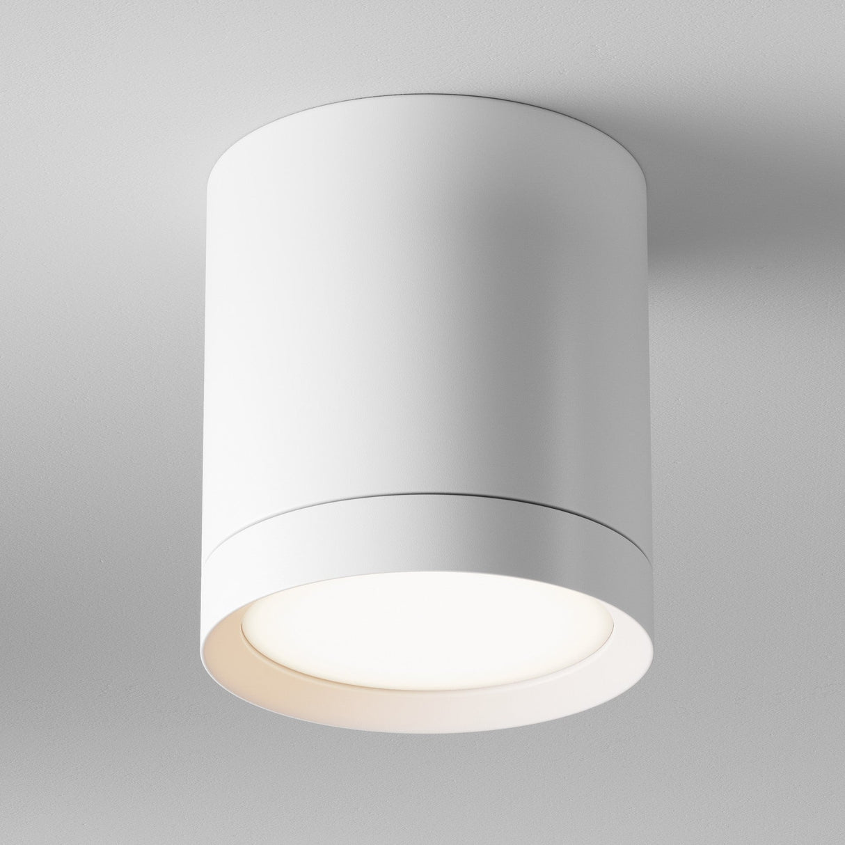 The Hoop Medium Round Surface Downlight - White is a sleek, cylindrical ceiling light with an integrated LED, offering soft, warm illumination. Its minimalist design seamlessly blends into modern spaces and white ceilings.