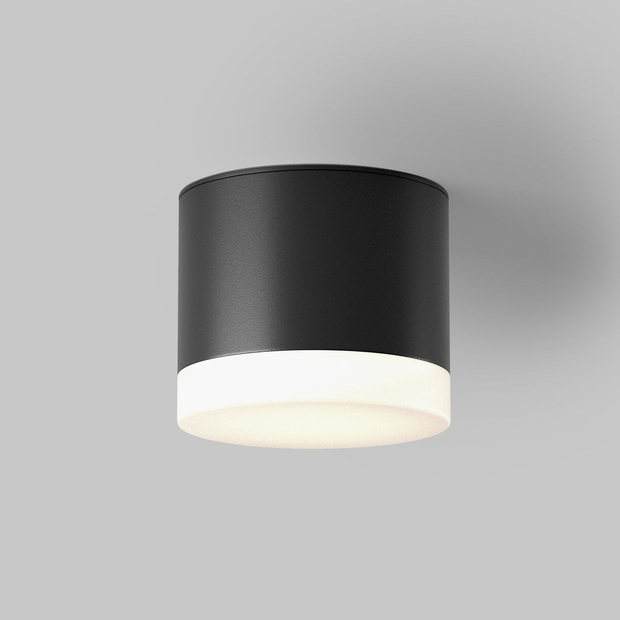 The Pauline Round Surface Downlight - Black, a sleek cylindrical ceiling light, enhances modern interiors with its matte black finish and frosted white diffuser against a light gray background.