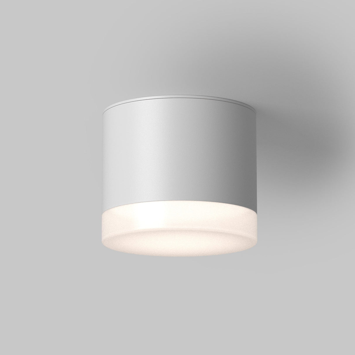 The Pauline Round Surface Downlight - White features a sleek, cylindrical matte white design. It emits a soft, warm glow against a pale gray background, making it an ideal modern lighting solution with minimalist charm.