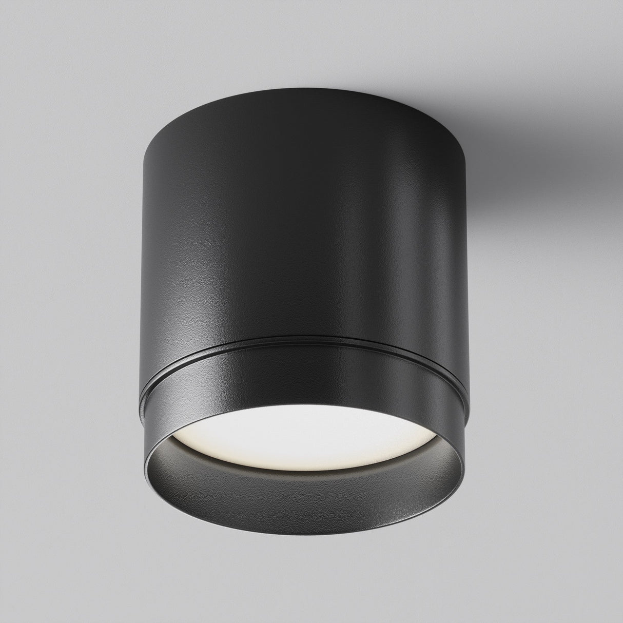 The Polar Round Surface Downlight - Black is a modern fixture with minimalist design, mounted on a white ceiling to emit a soft, diffused glow. Its sleek cylindrical shape enhances contemporary interiors.