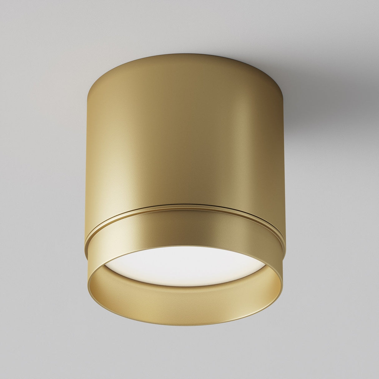 The Polar Round Surface Downlight - Matte Gold has a minimalist design and is mounted on a white ceiling, emitting a soft, warm glow from its round opening, ideal for accent lighting.