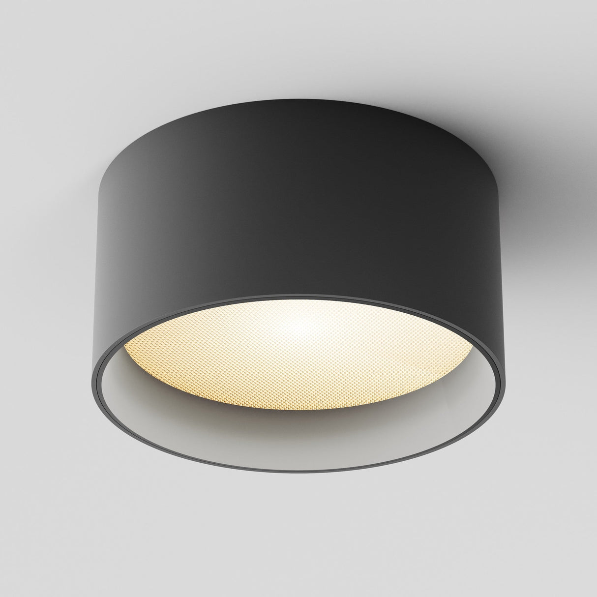 The Vega LED Round Surface Downlight 15W 3000K - Black, with its modern cylindrical design and matte black finish, emits warm yellow light from a white ceiling, illuminating the space softly.