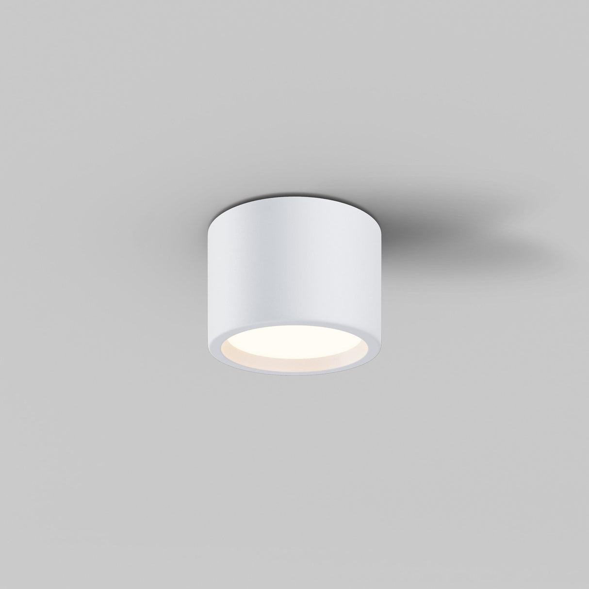 The Hydra LED Round Surface Downlight 10W 3000K - White is mounted against a gray background, softly emitting a warm glow downward with its IP44 rating, creating a gentle ambiance.