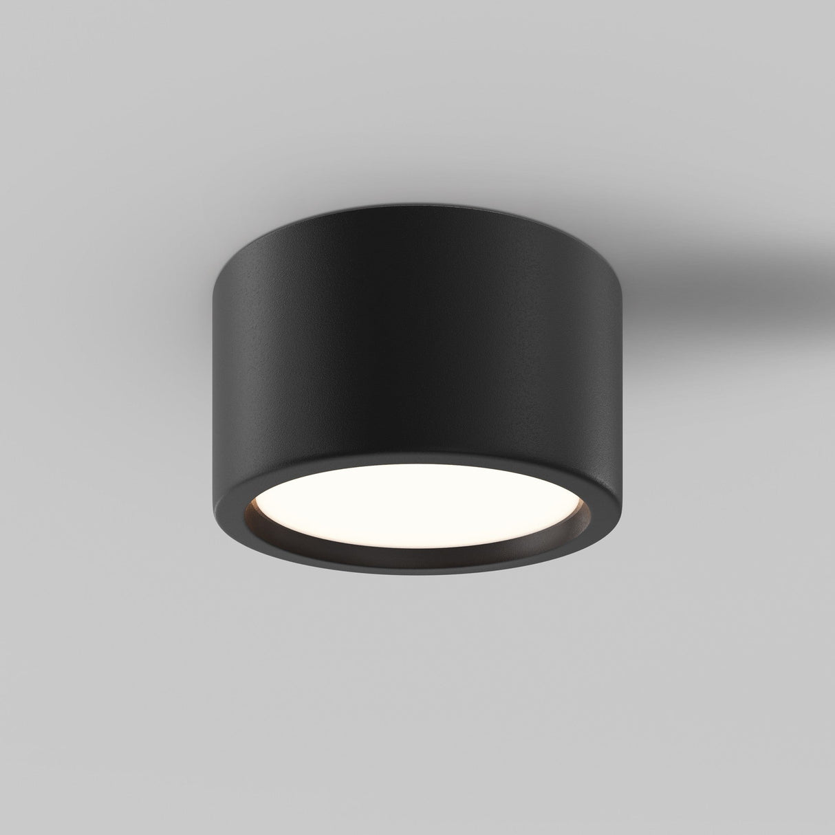 The Hydra LED Round Surface Downlight 15W in black is a modern cylindrical fixture on a white ceiling. It emits a soft 3000K glow, boasts an IP44 rating for durability, and features a sleek, minimalistic design ideal for various interiors.
