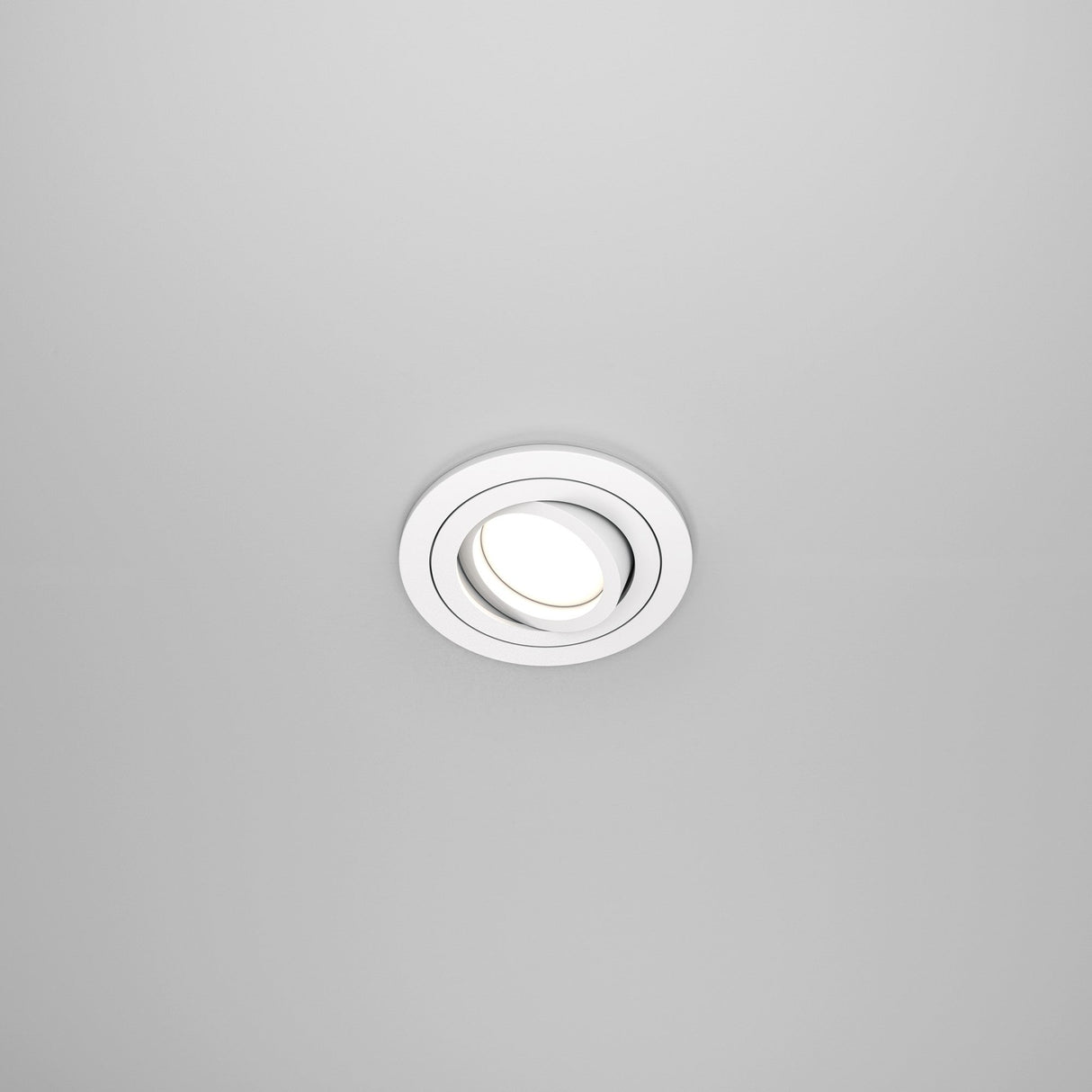 The Atom Single Tilt Round Recessed Downlight - White (DL023-2-01W) features a sleek, modern circular design that provides a minimalist look while illuminating against a plain, light gray ceiling.