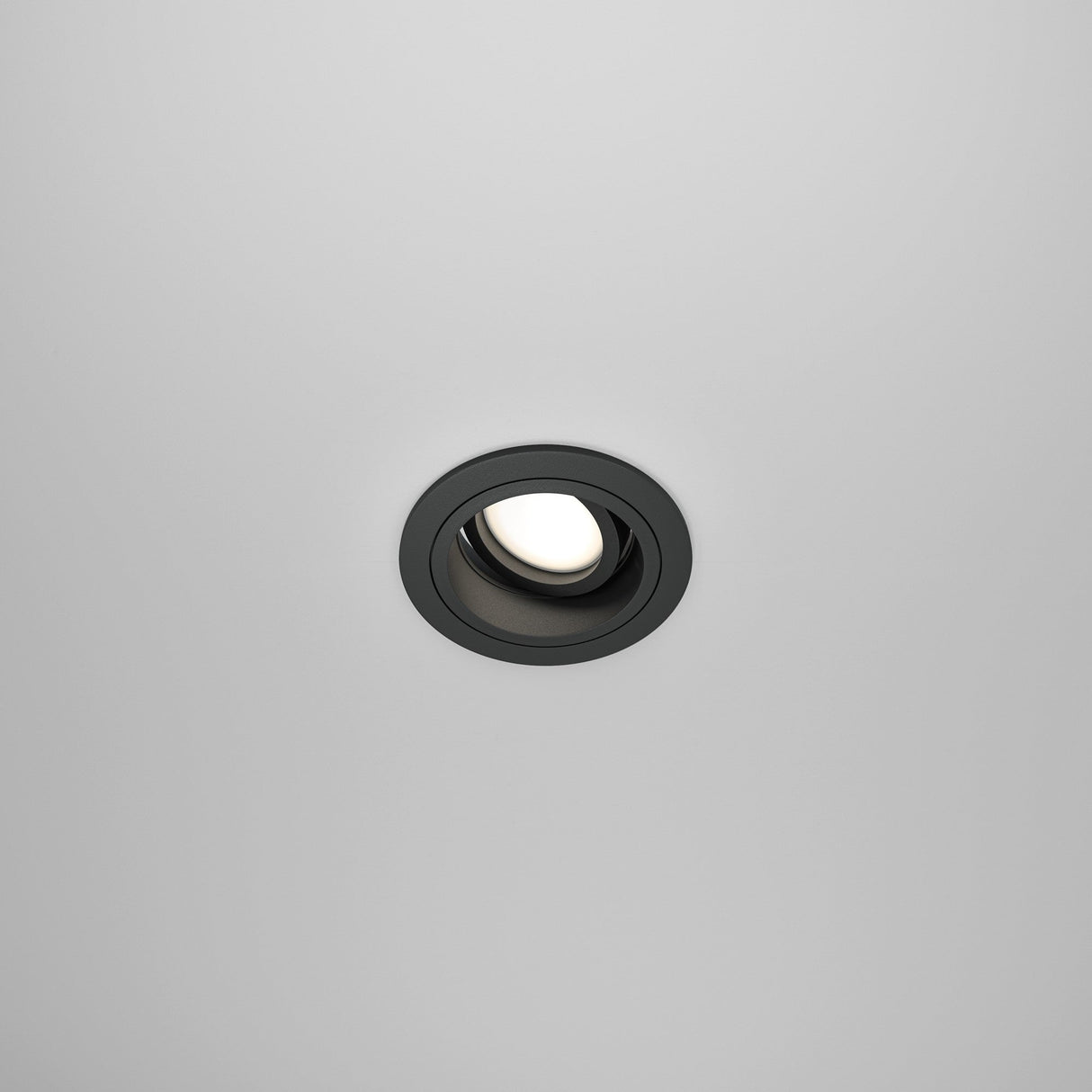 The white ceiling features the Atom Single Tilt Round Recessed Downlight in black, which adds a modern touch. This recessed fixture has an adjustable tilt and emits a soft glow when turned on.