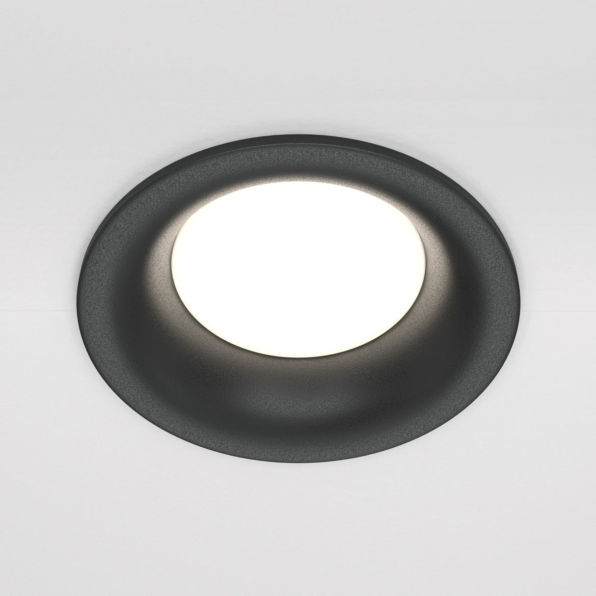 The Slim Fixed Round Recessed Downlight - Black provides a bright white glow on a plain white ceiling, combining modern elegance with its sleek black finish.