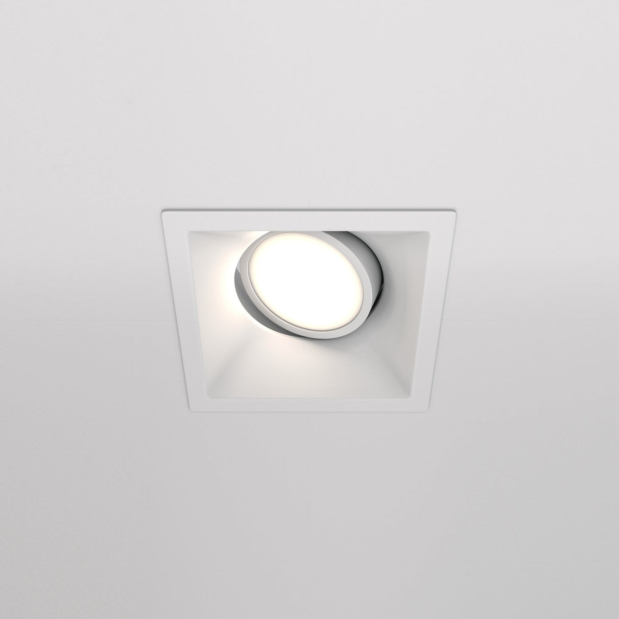 The Dot Single Tilt Square Recessed Downlight features a circular LED bulb casting a soft glow, installed within a white ceiling.