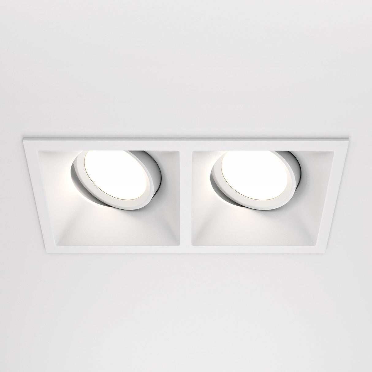 A white ceiling showcases two recessed Dot Twin Tilt Rectangular Downlights, each with circular lights. These fixtures offer a soft glow, highlighting a minimalist, modern aesthetic while being energy-efficient.