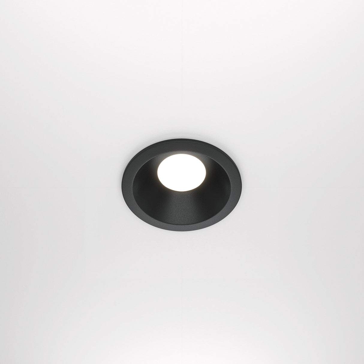 The Zoom Single Fixed Round Recessed Downlight - Black features a circular black cast aluminium fixture and a bright white LED bulb, blending seamlessly into a smooth white ceiling. It offers both style and durability with its IP65 rating.