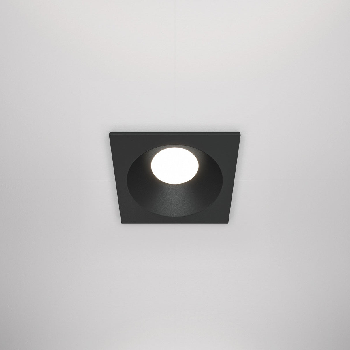 The Zoom Single Fixed Square Recessed Downlight - Black features a central circular bulb, a minimalist black finish for modern appeal, complements any white ceiling, and offers durability with an IP65 protection rating.
