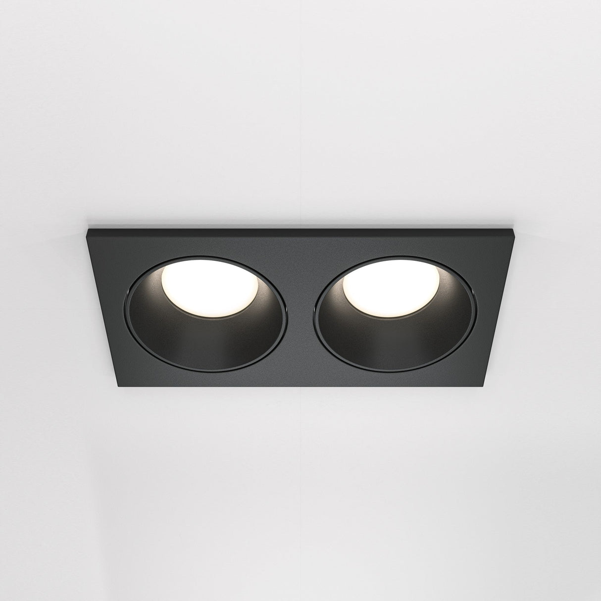 The Zoom Twin Fixed Rectangular Recessed Downlight in black features two circular LED lights elegantly embedded in a white ceiling, offering a modern design with an IP65 rating for enhanced durability.