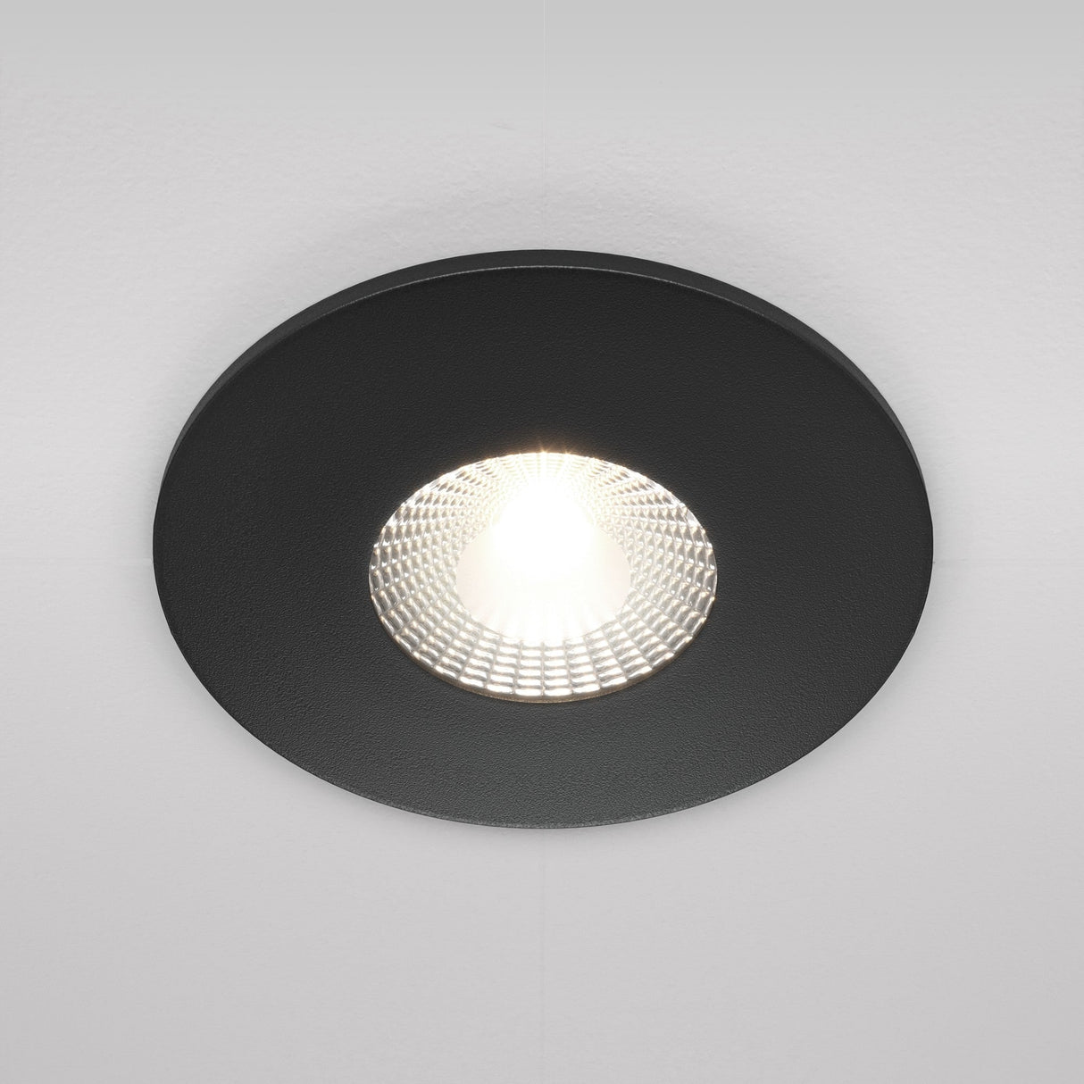 The Zen LED Round Recessed Downlight 7W 4000K - Black casts an energy-efficient, focused beam. Its interior texture enhances the effect against a white ceiling.