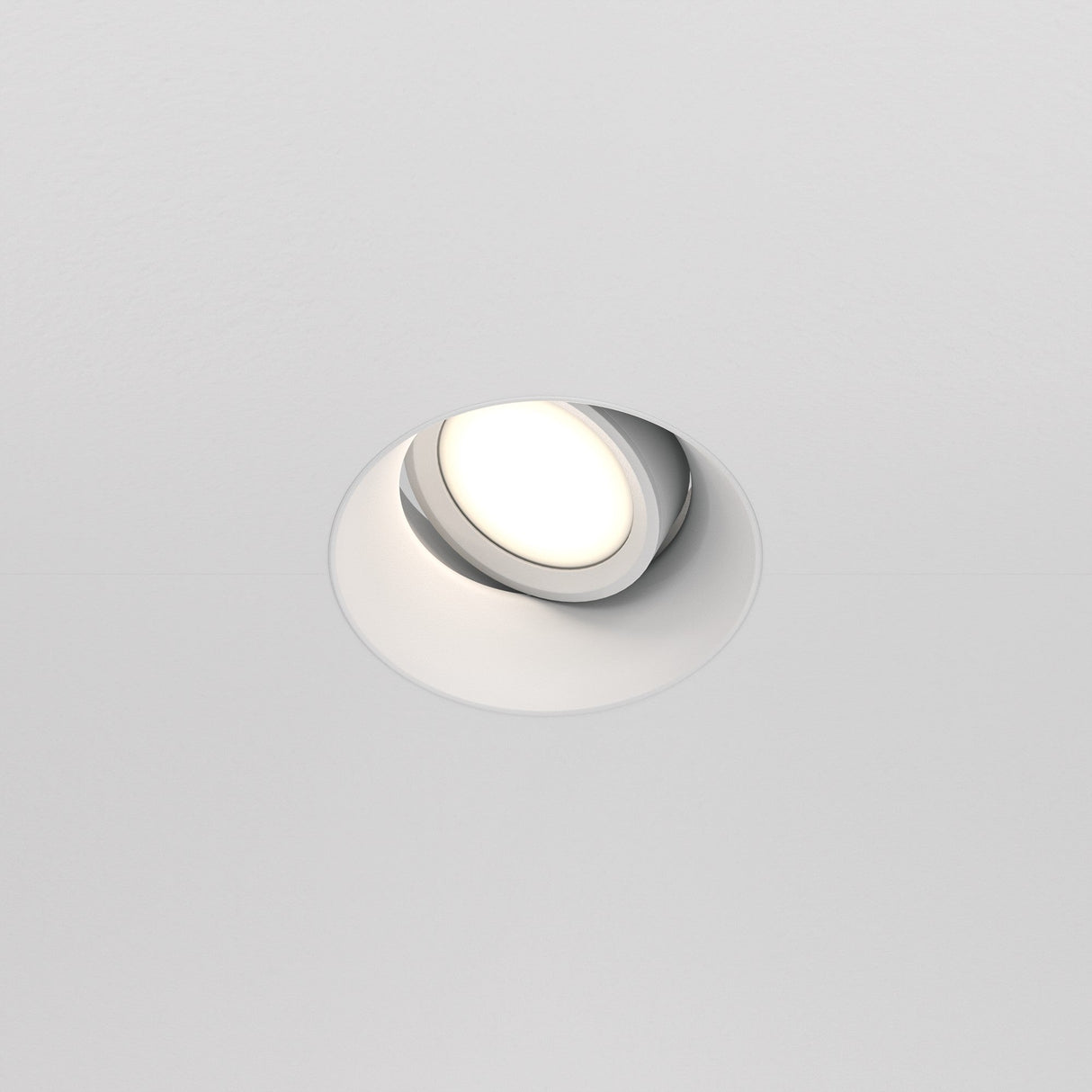 The Dot Single Tilt Plaster-in Round Recessed Downlight in white, embedded in the ceiling, is turned on, emitting a soft, warm glow with its adjustable tilt mechanism providing directional illumination.