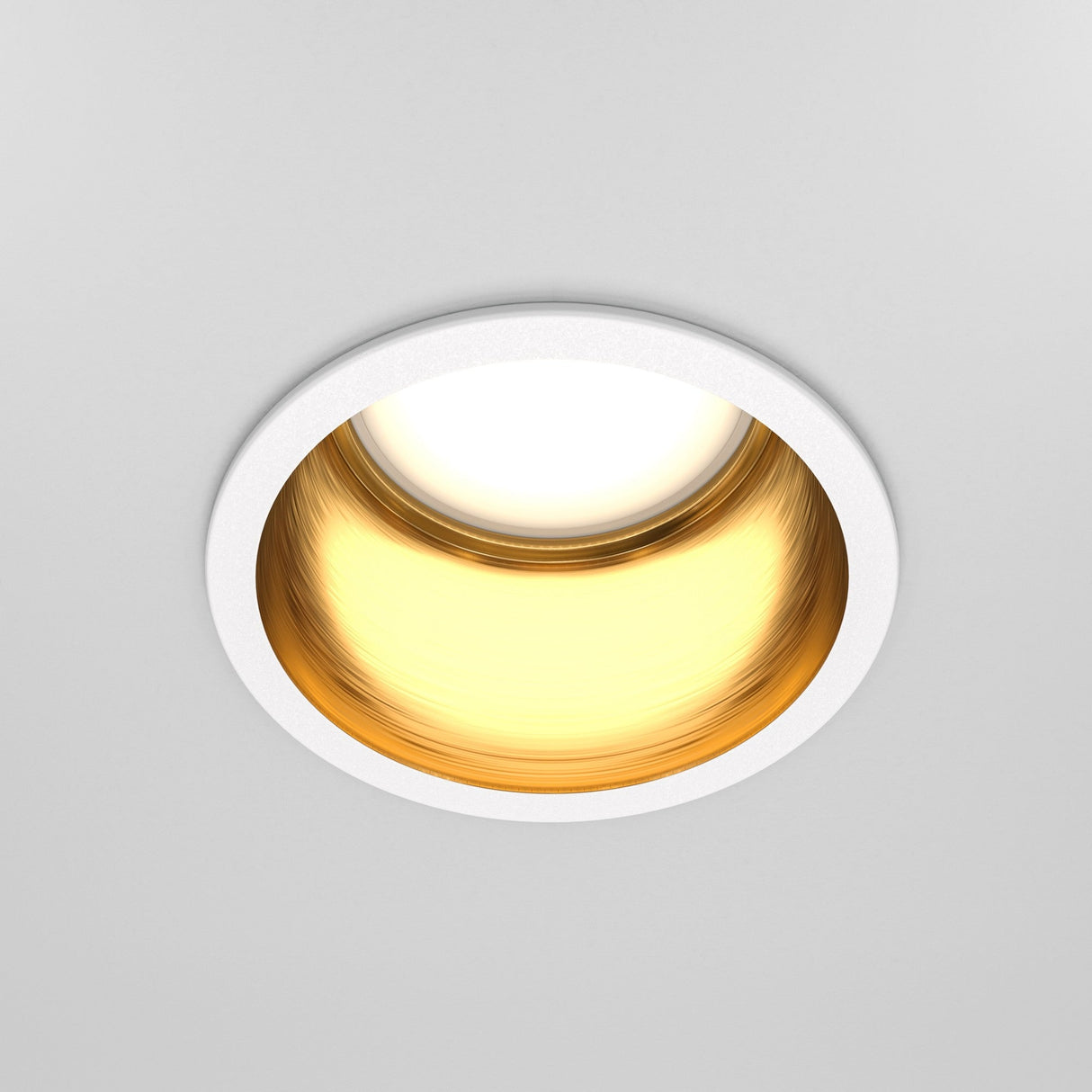 The Reif Round Recessed Downlight features a white trim and reflective golden interior, emitting ambient lighting with a warm glow that beautifully contrasts the white exterior and lustrous gold finish, adding elegance to any space.