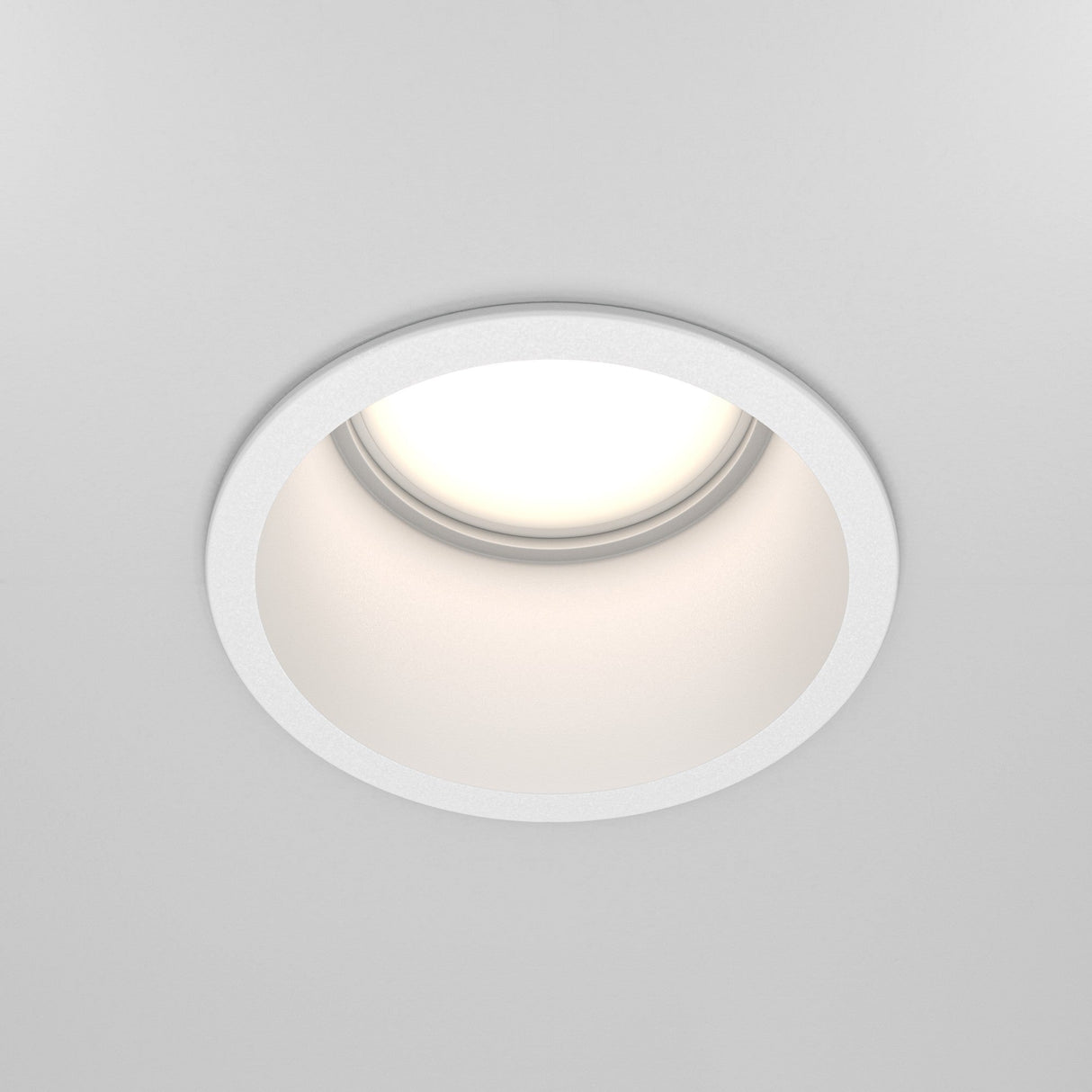 The Reif Round Recessed Downlight - White, crafted from high-quality materials, is installed in a white ceiling and emits soft, bright light ideal for modern spaces.