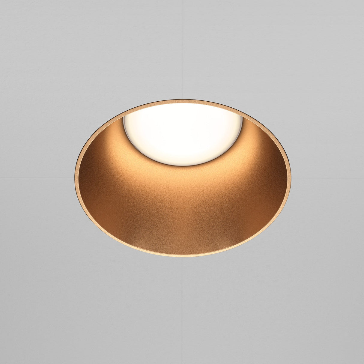 The Share Round Plaster-in Fixed Recessed Downlight in matte gold adds a soft, warm glow against a neutral gray ceiling with its circular design and seamless plaster-in installation.