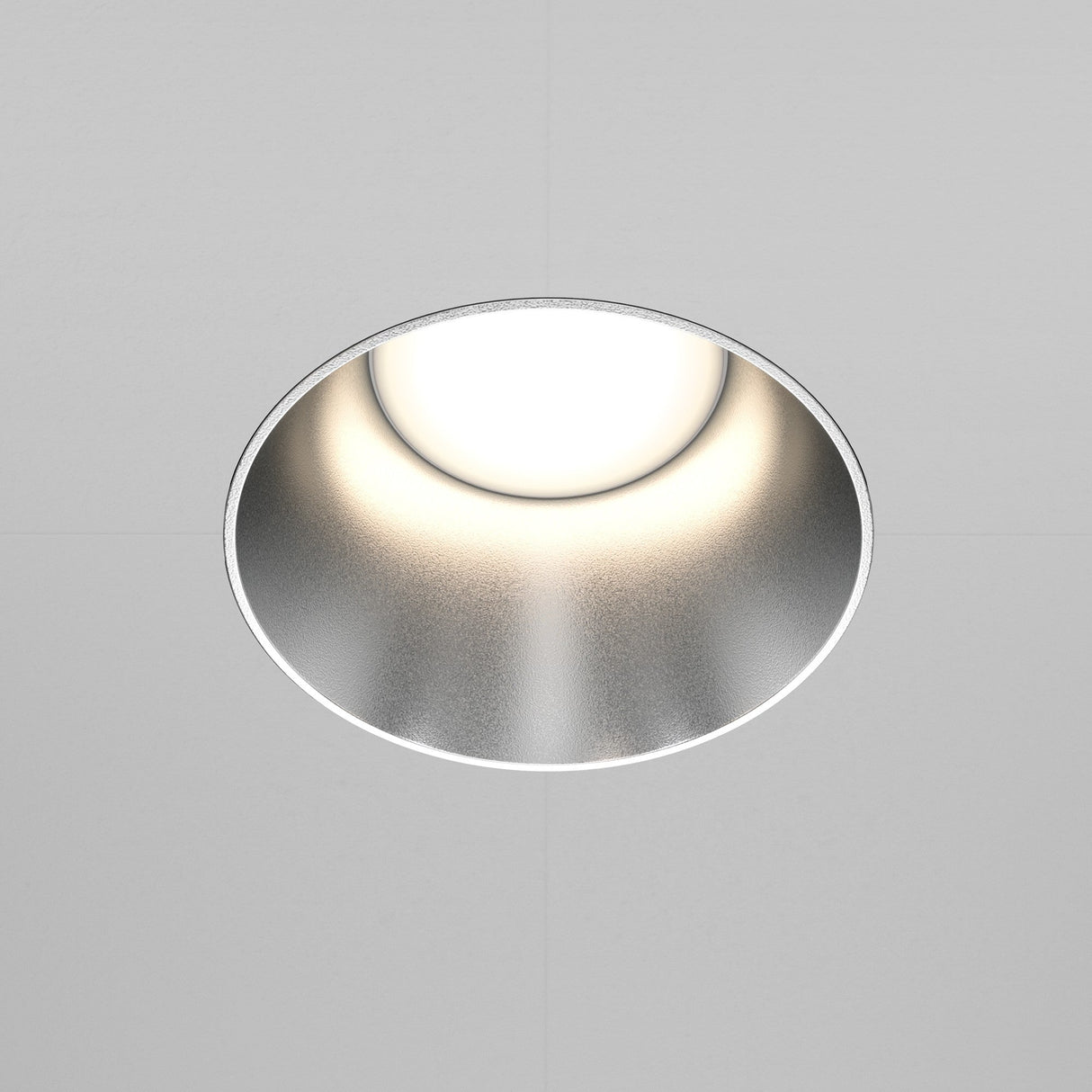 The Share Round Plaster-in Fixed Recessed Downlight, boasting a minimalist design, features a matte silver finish and a glowing white center against a plain white ceiling.