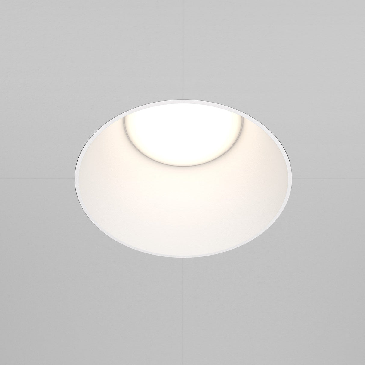 The Share Round Plaster-in Fixed Recessed Downlight - White, with its minimalist round design, casts a soft glow, enhancing the understated elegance of the surrounding white ceiling.