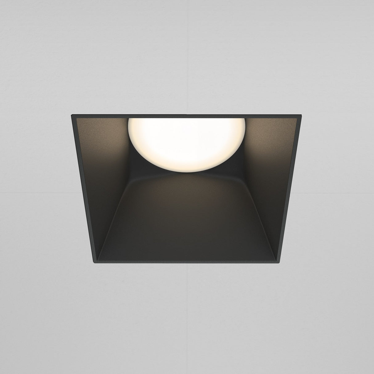 The Share Square Plaster-in Fixed Recessed Downlight - Black, offers a modern square design with a circular glowing center, set in black angled housing for plaster-in installation against a light gray background.
