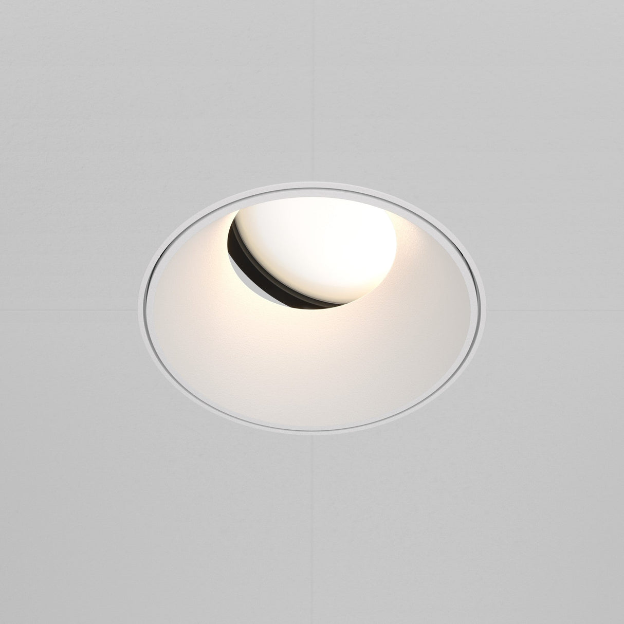 The Share Round Plaster-in Recessed Swivel Downlight in white has a circular trim with a slightly angled bulb for a soft glow. Embedded in a smooth white ceiling, it offers adjustable light direction for versatile illumination.